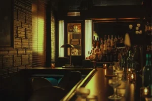 Dimly lit bar with rows of bottles and a lit glass-front cabinet behind the counter