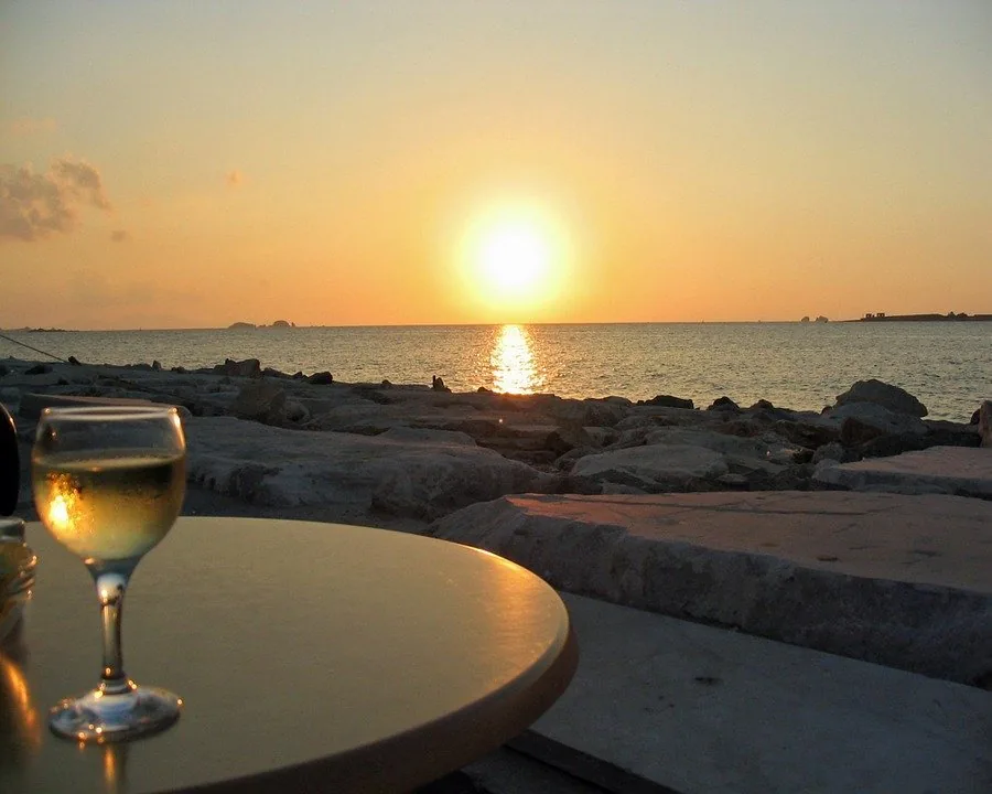 Glass of white wine on a table by the sea as the sun sets over the water