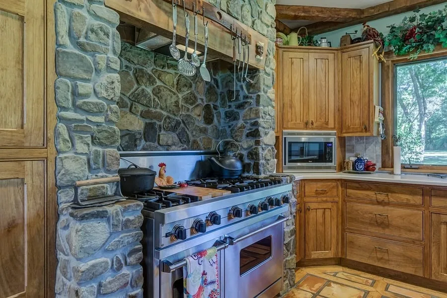 Rustic kitchen with a stainless steel gas range set in a stone alcove beside wood cabinets