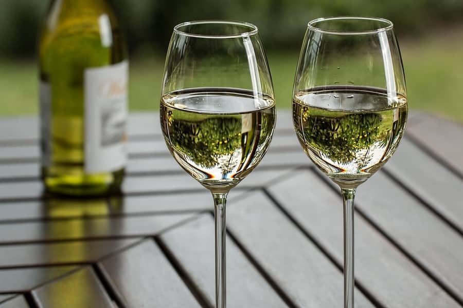 Two glasses of chilled white wine on a wooden outdoor table beside an open bottle