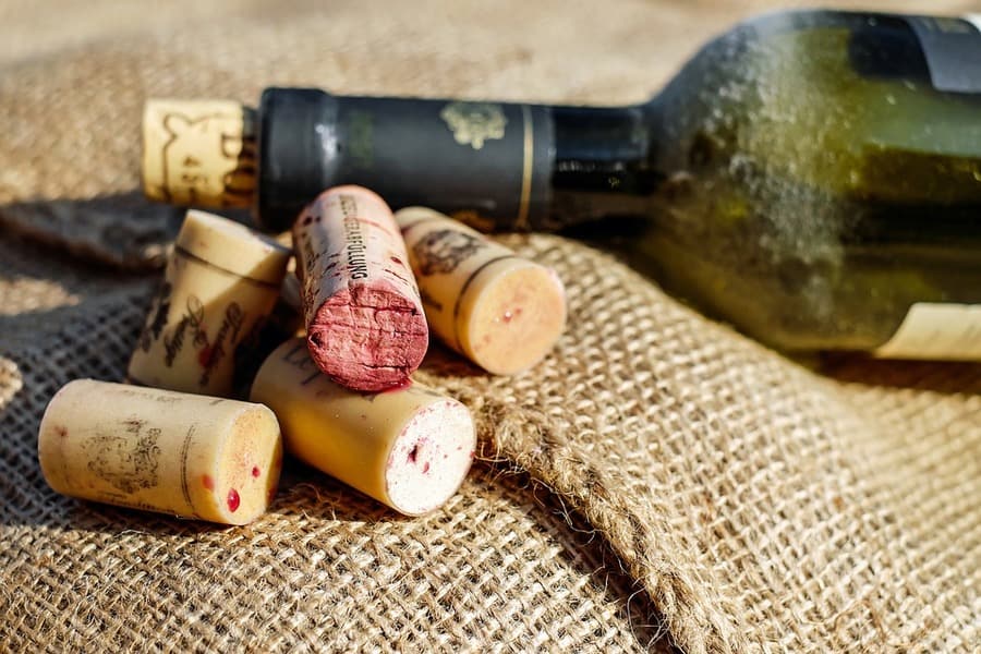 Used wine corks, some stained red, beside a green wine bottle lying on burlap