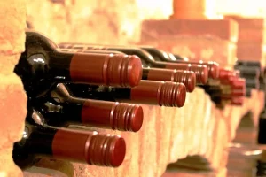 Wine bottles resting horizontally in stone cellar niches with red wax capsules facing out