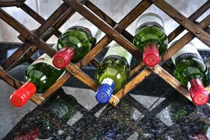 Green wine bottles resting on their sides in a wooden lattice wine rack on a granite counter