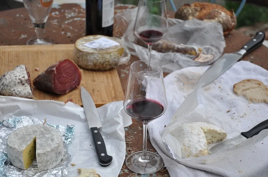 Rustic table with aged cheeses, cured meat, bread and two glasses of red wine