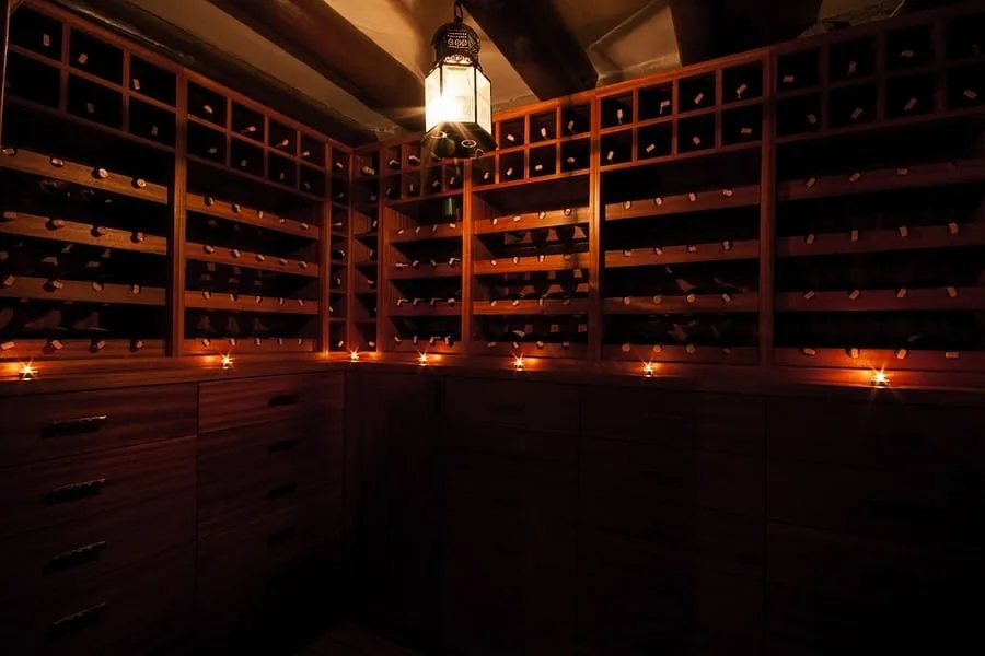 Dim wine cellar lined with wooden bottle racks, drawer cabinets and candles under a hanging lantern