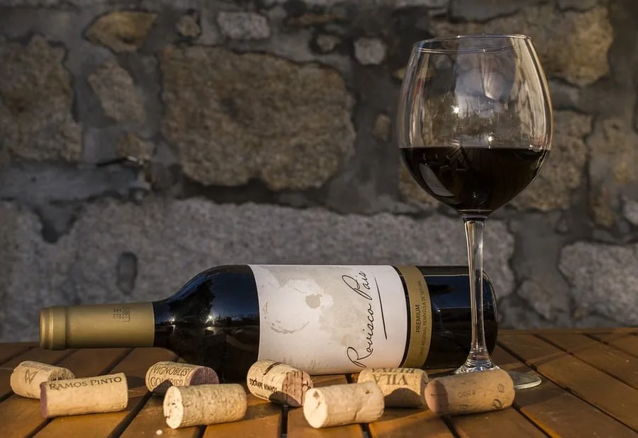 Red wine bottle lying on a wooden table with scattered corks and a filled glass