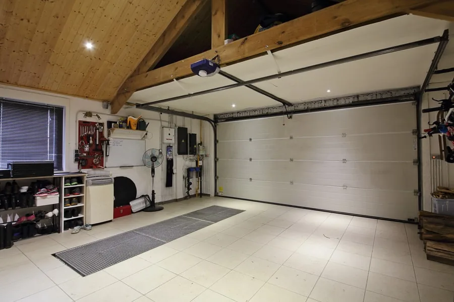 Empty two-car home garage with tiled floor, closed door and wood ceiling, a common wine storage spot