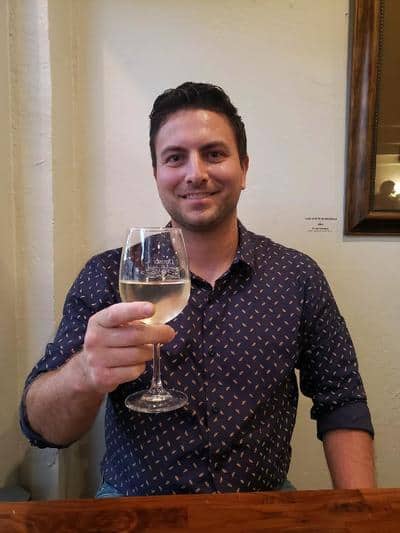 A smiling man raises a glass of white wine in a tasting room