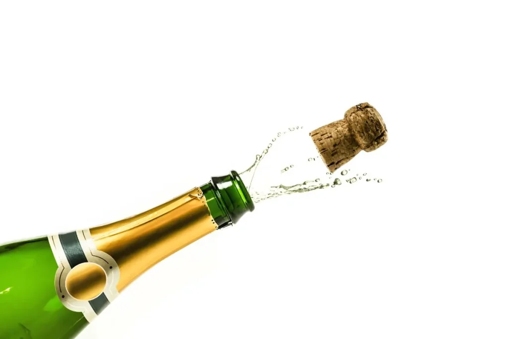 Green sparkling wine bottle with the cork popping out and wine spraying from the neck
