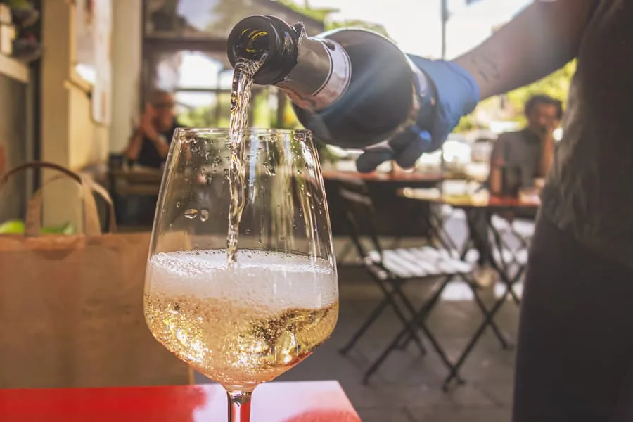 Sparkling wine being poured into a stemmed glass at an outdoor cafe table