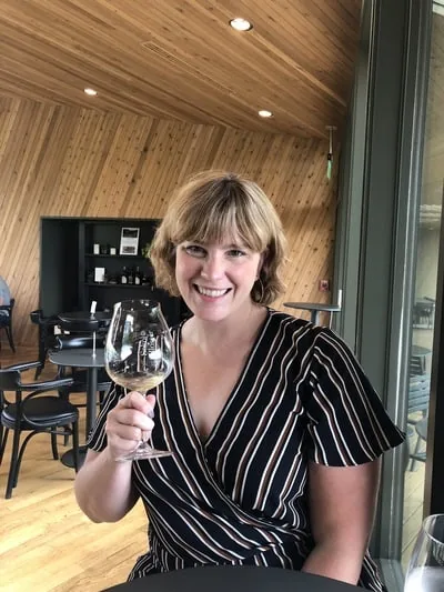 A smiling woman raises a glass of white wine in a wood-paneled tasting room