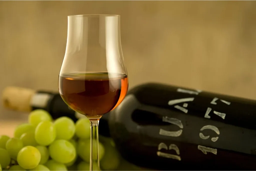 Amber fortified wine in a tulip glass beside a dark aged bottle and green grapes