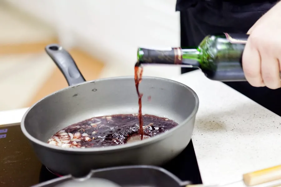 Red wine poured from a bottle into a skillet with chopped onions for a pan sauce