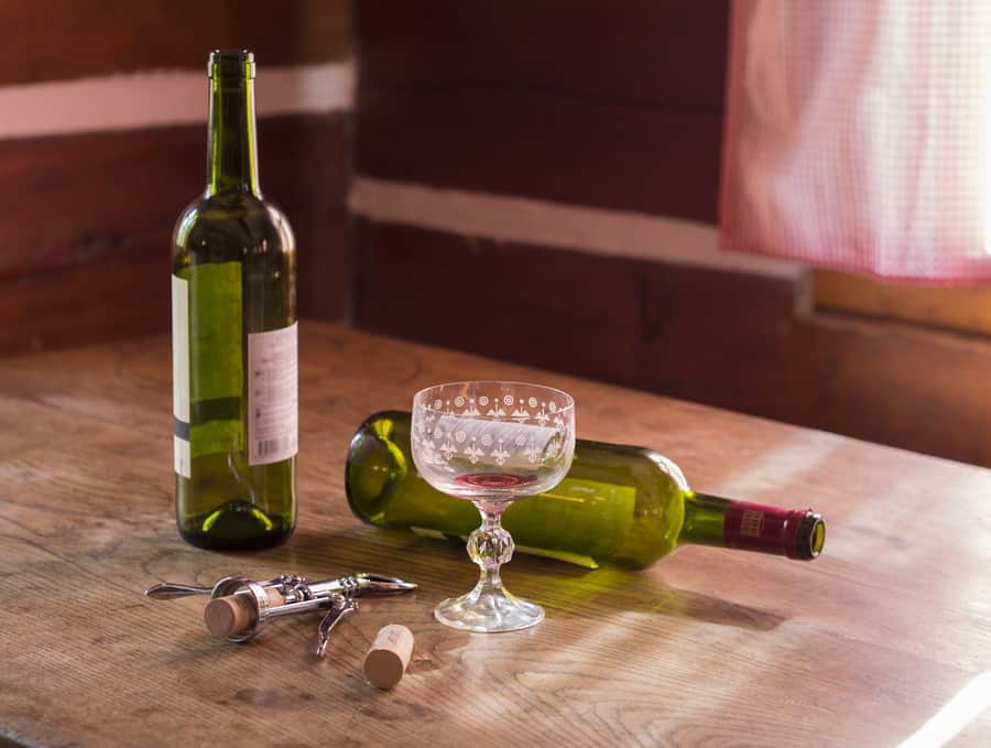 Two empty green wine bottles with corks, a corkscrew and an etched glass on a wooden table