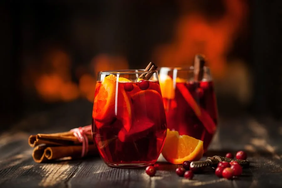 Two glasses of mulled wine with orange slices, cranberries and cinnamon sticks by a fire