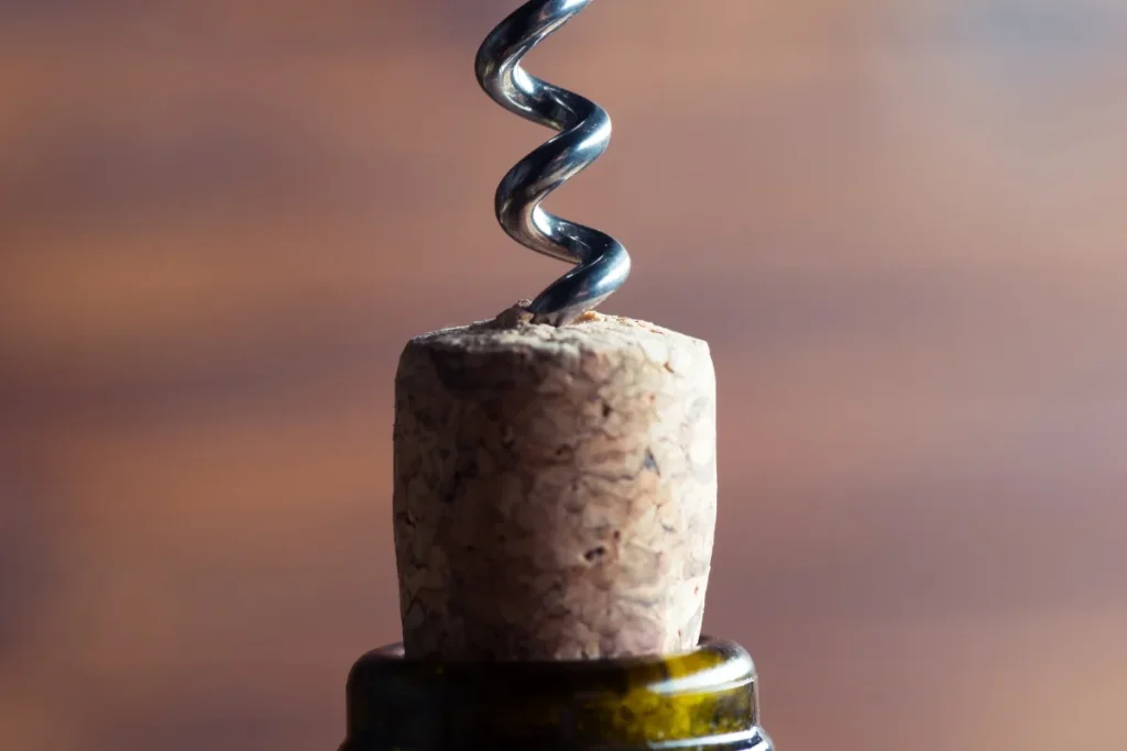 Corkscrew worm threaded into a natural cork being pulled from a wine bottle neck