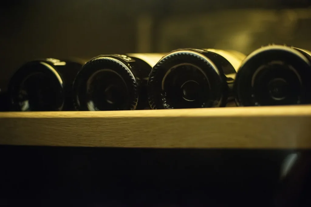 Dark wine bottles resting on their sides on a wooden rack in dim light