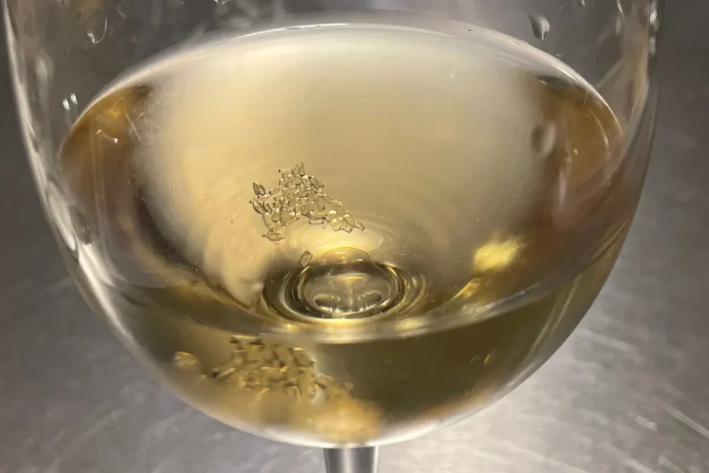 Close-up of tiny wine crystals settled at the bottom of a glass of white wine
