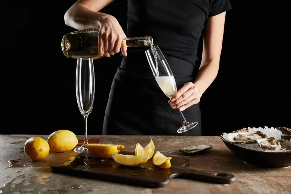 Sparkling wine poured into a flute beside lemons and oysters on ice