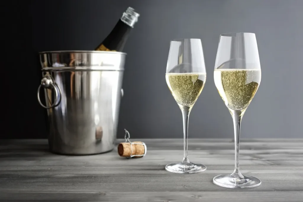 Two glasses of sparkling wine beside a bottle chilling in a stainless steel ice bucket
