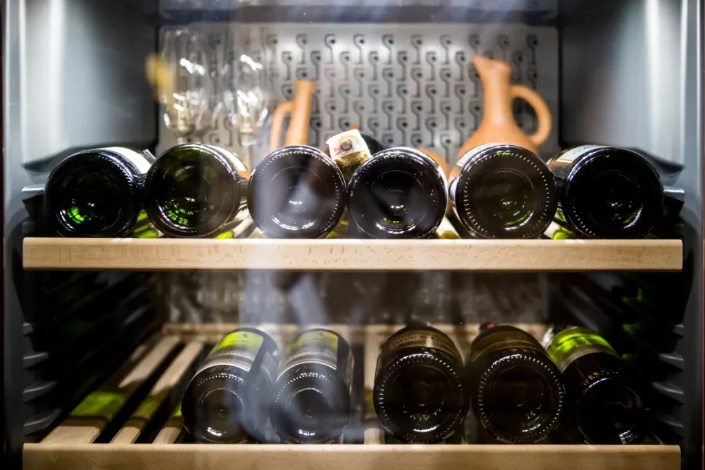 Wine bottles resting on wooden shelves inside a cooled wine fridge