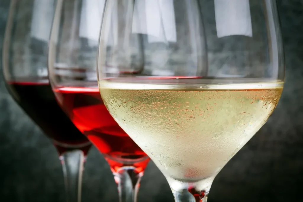 Three wine glasses holding chilled white, rose and red wine, with condensation on the white