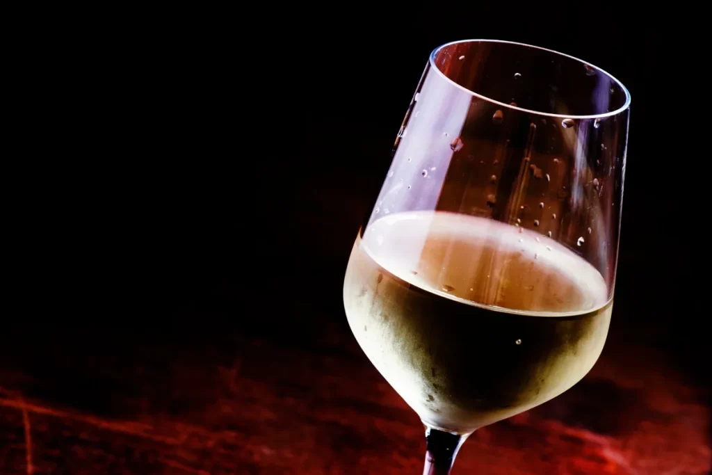 Glass of chilled white wine with condensation on the bowl against a dark background