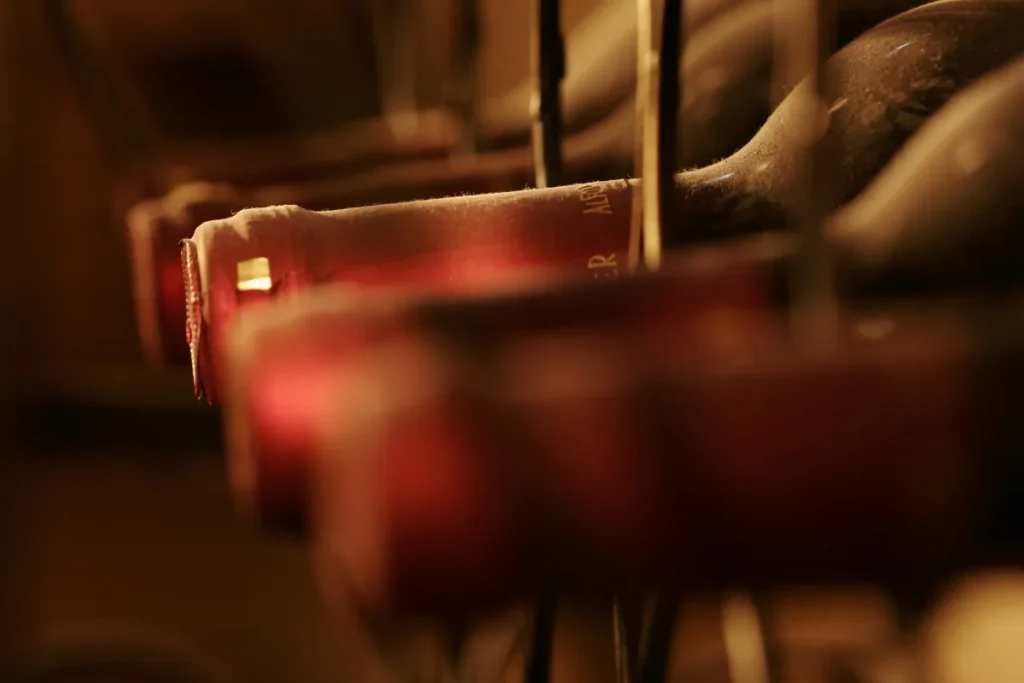 Dusty red wine bottles resting on their sides in a dim cellar rack