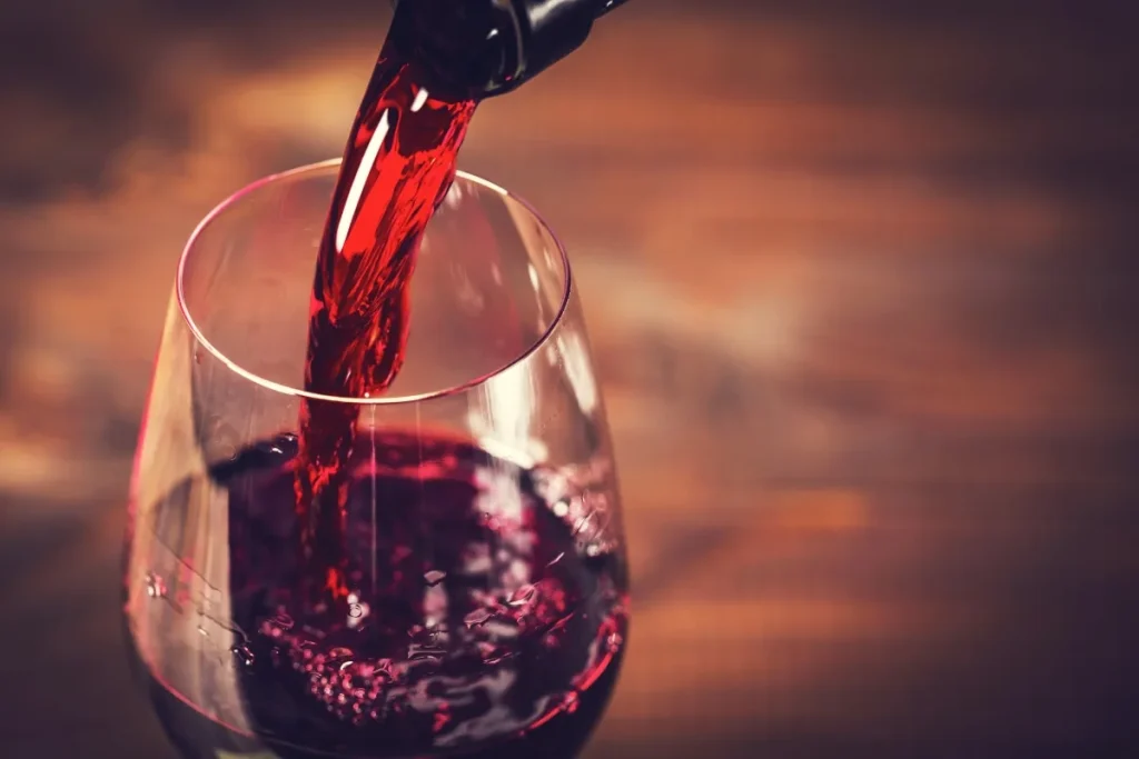 Red wine pouring from a bottle into a stemmed glass on a wooden table