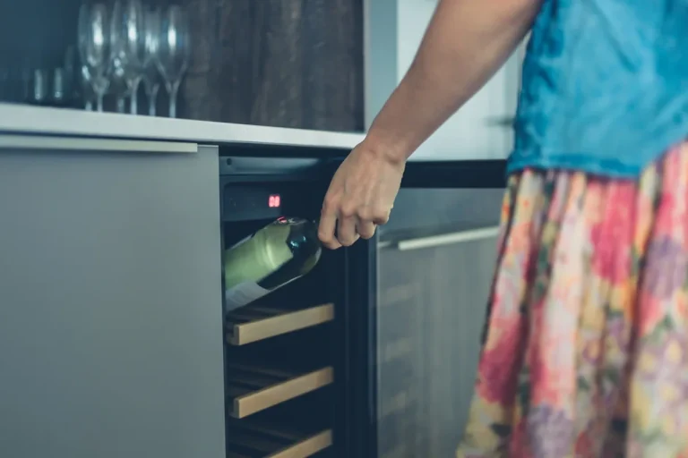 A woman places a wine bottle on the wooden shelf of an undercounter wine fridge with a lit display