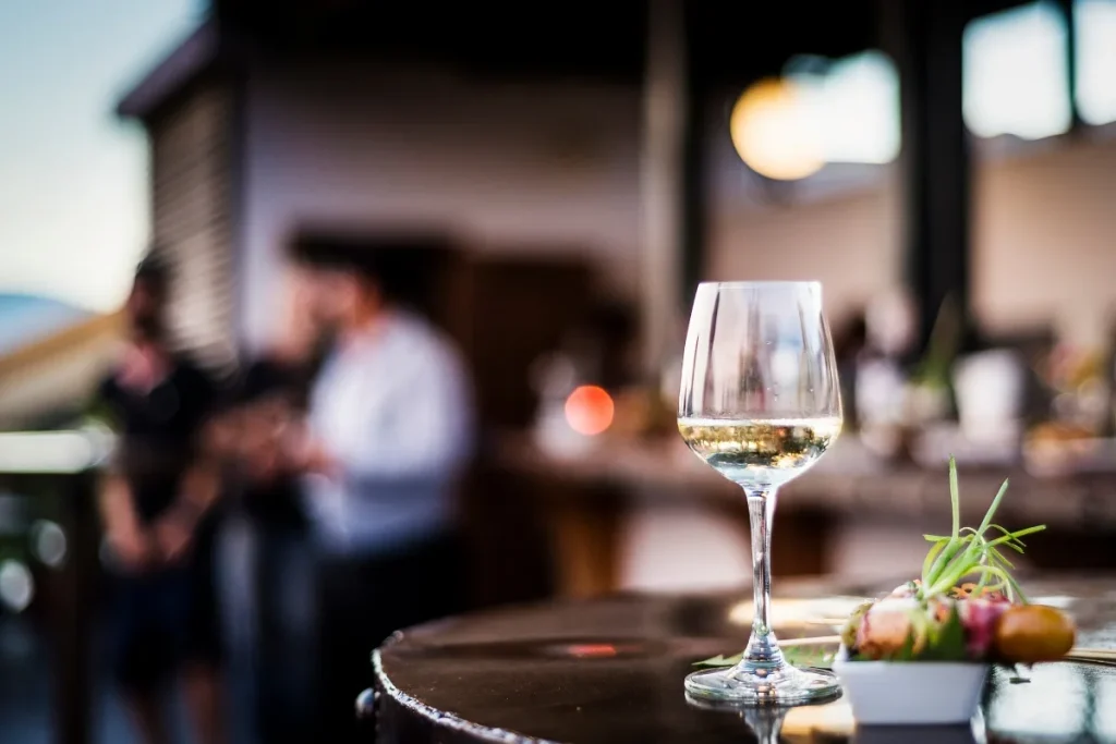 Glass of chilled white wine on a barrel table at an outdoor tasting bar with small plate of food