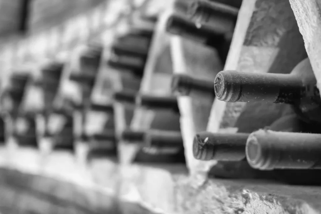 Dusty old wine bottles resting on their sides in a stone cellar rack