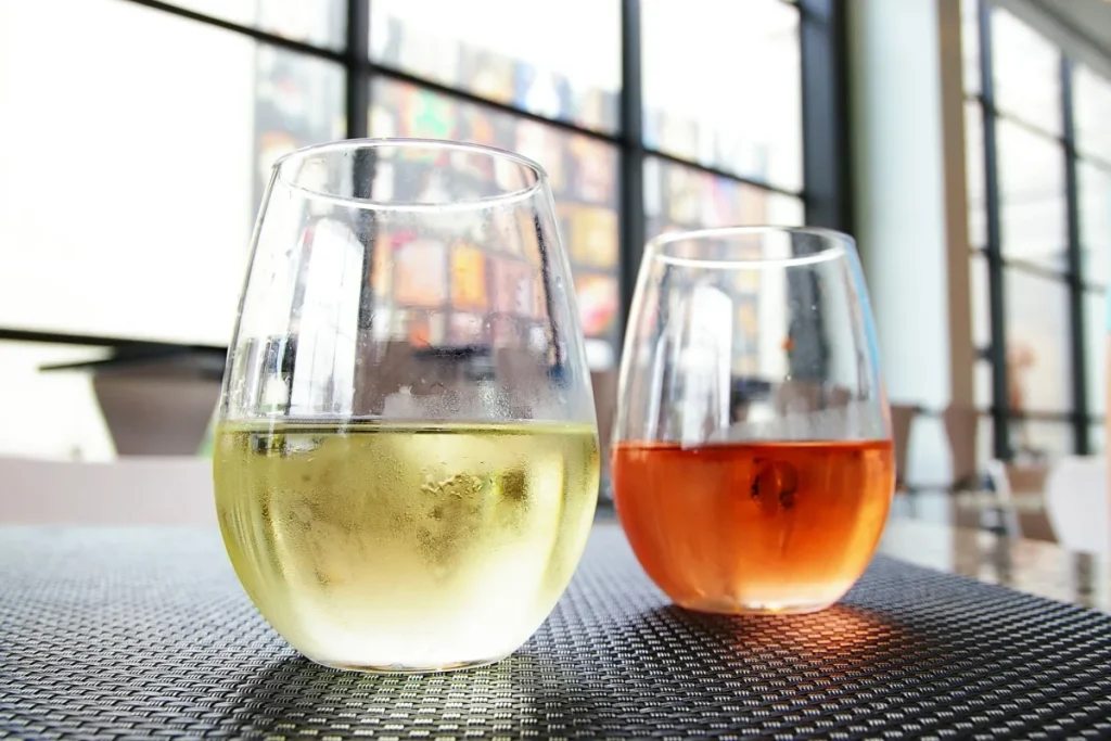 Two stemless wine glasses of chilled white and rose wine on a woven table mat