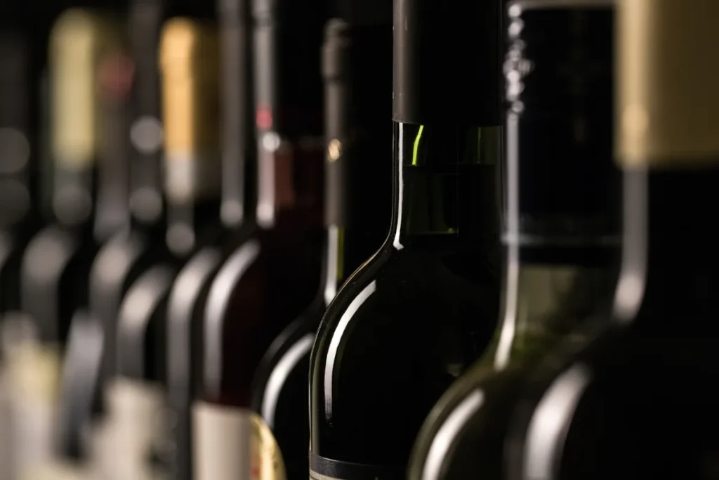 Row of sealed dark wine bottles resting in a dim cellar, where unopened wine ages slowly