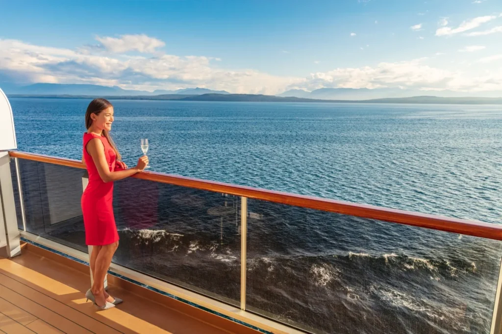 A woman in a red dress holds a wine glass at a cruise ship railing overlooking the ocean