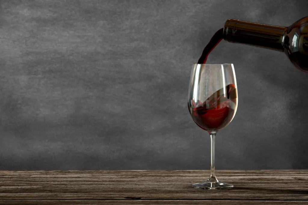 Red wine poured from a dark bottle into a stemmed glass on a wooden table