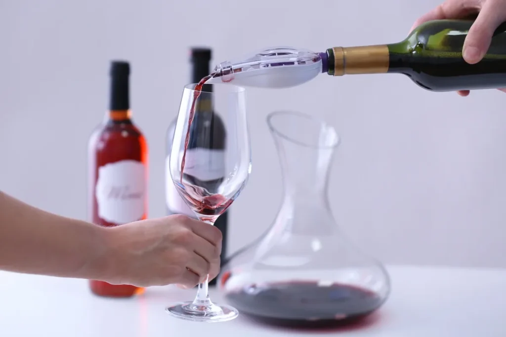 Red wine poured through a bottle aerator into a glass next to a glass decanter