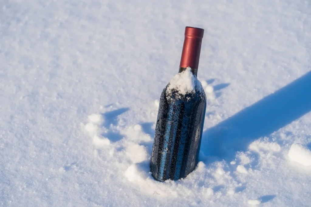 Unlabeled wine bottle with red foil capsule buried upright in snow and covered in frost