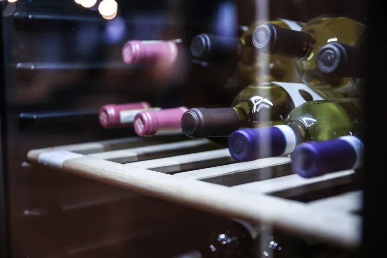 Wine bottles lying on their sides on a wooden shelf inside a wine cooler