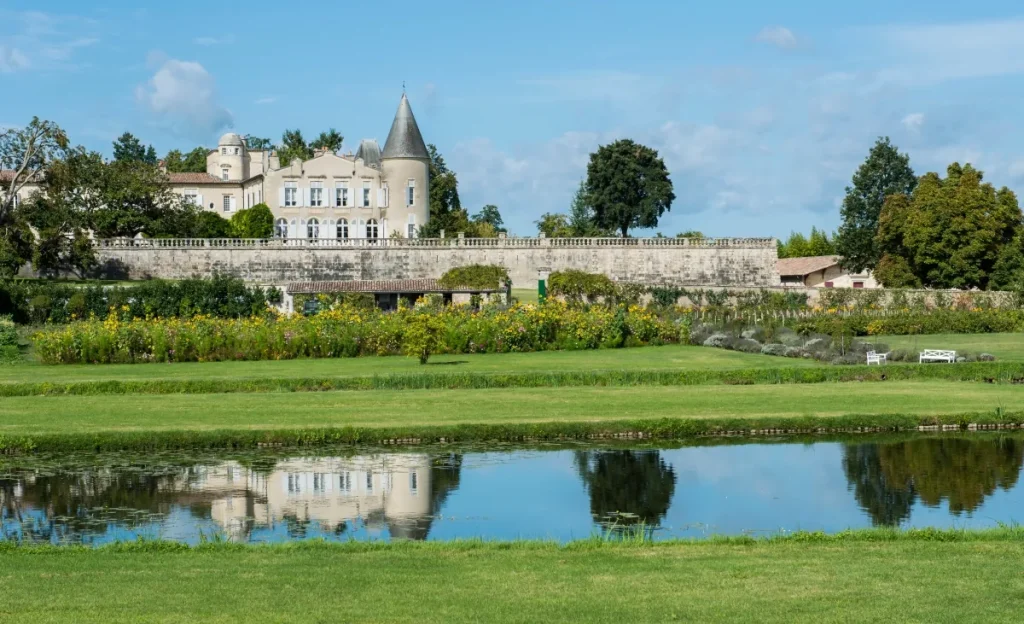 Historic stone chateau with a turret behind garden walls, reflected in a still pond