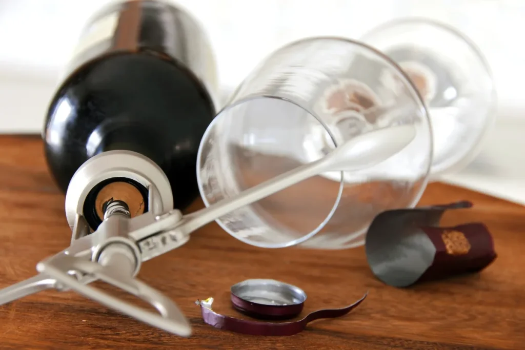 Cut foil capsule and corkscrew beside a wine bottle and tipped glass on a wooden table