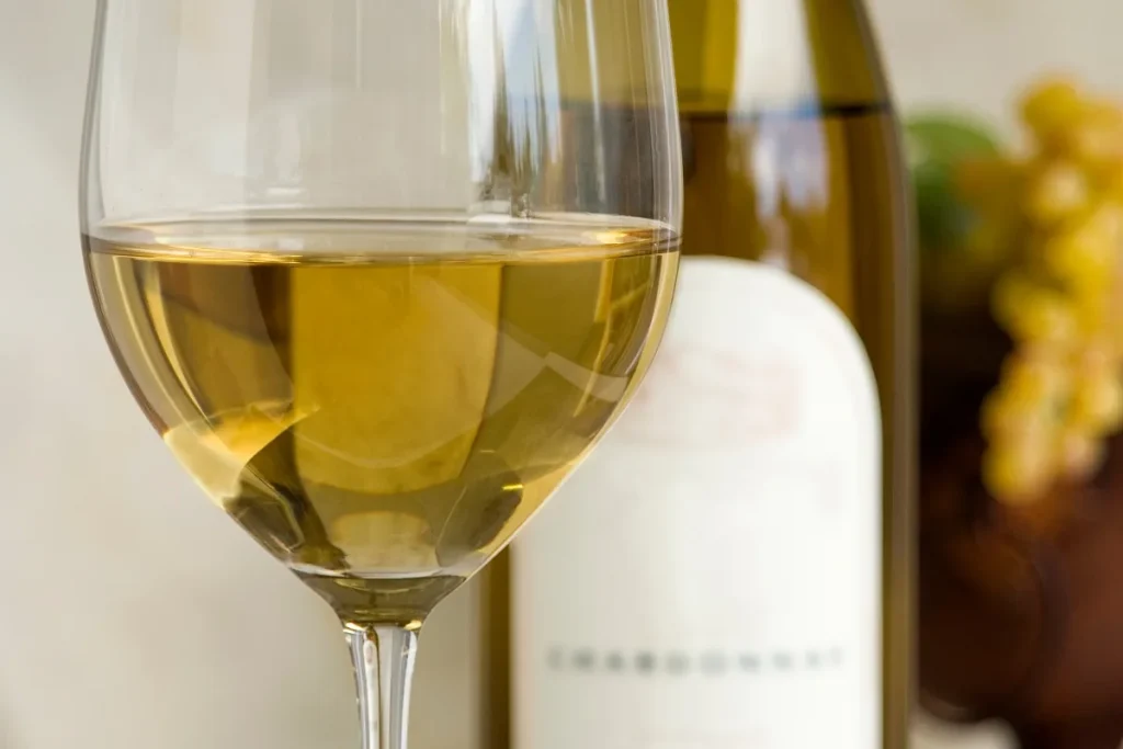 Glass of pale gold Chardonnay next to a bottle labeled Chardonnay and green grapes