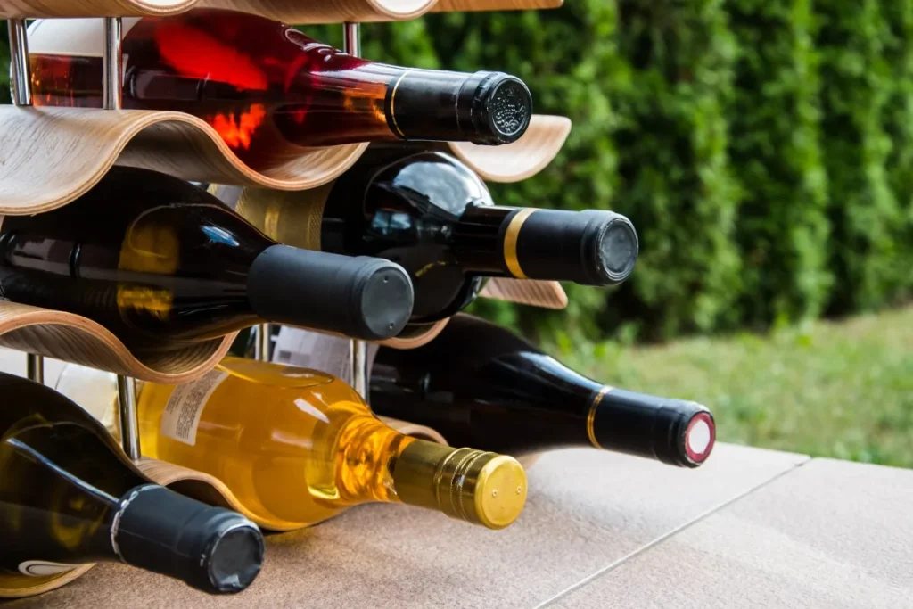 Red, white and rose bottles resting on their sides in a wavy wooden rack outdoors
