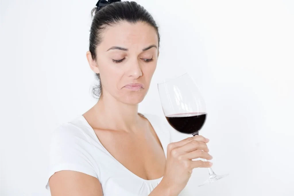 A woman grimaces as she looks at a glass of red wine, suggesting it has spoiled