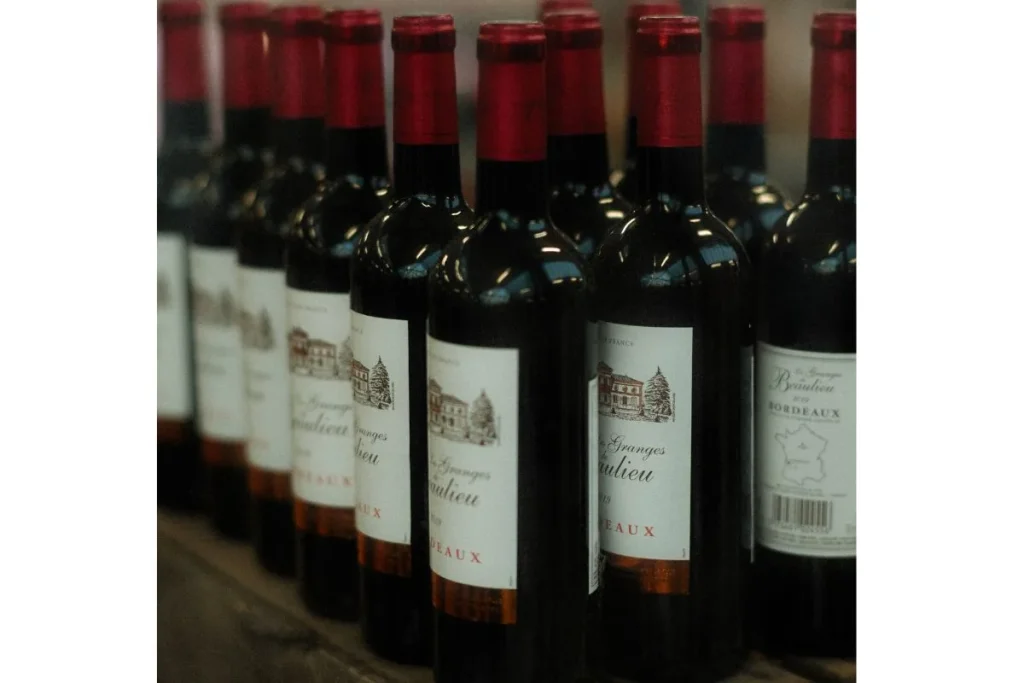 Rows of red wine bottles labeled Bordeaux standing close together on a wooden surface
