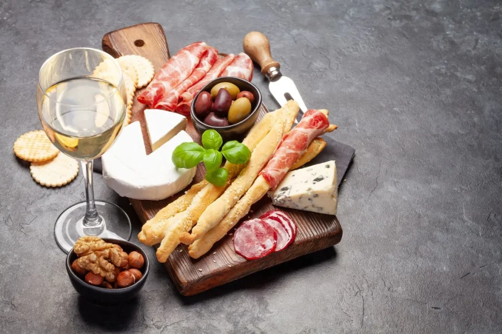 Charcuterie board with cured meats, soft and blue cheese, olives and a glass of white wine
