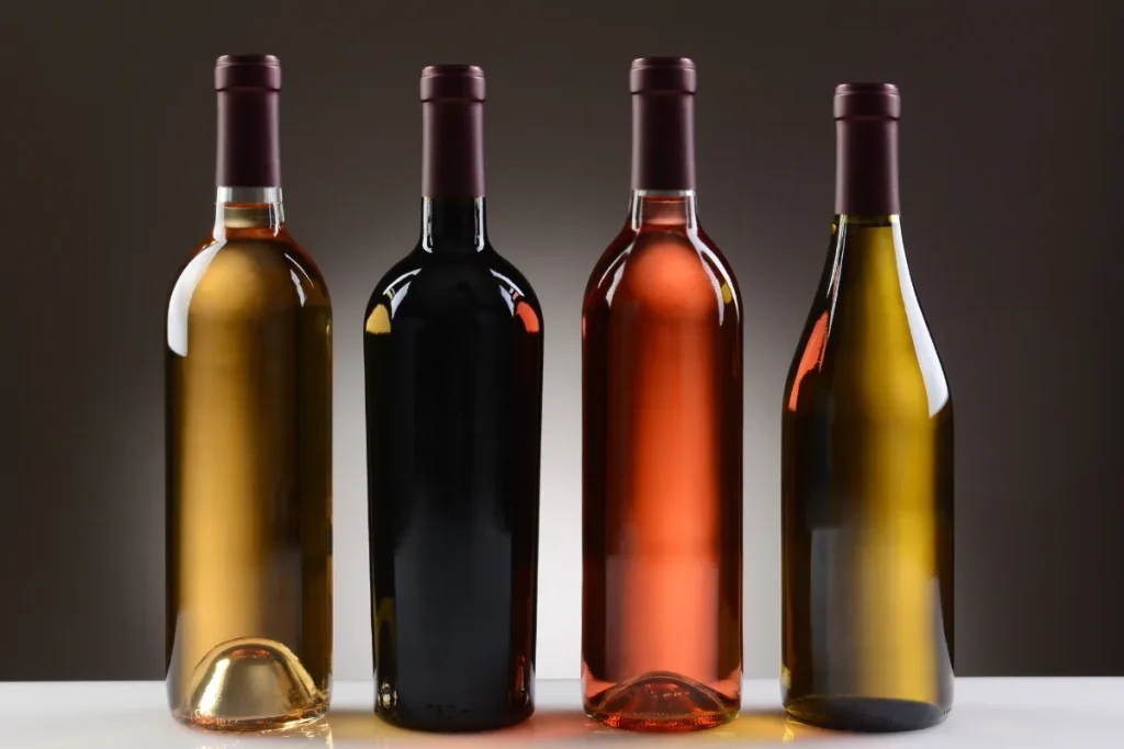 Four unlabeled wine bottles holding white, red, rose and golden wine side by side