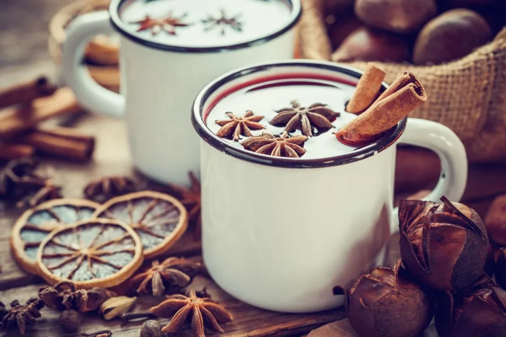 Two enamel mugs of mulled wine topped with star anise and cinnamon sticks on a wooden table