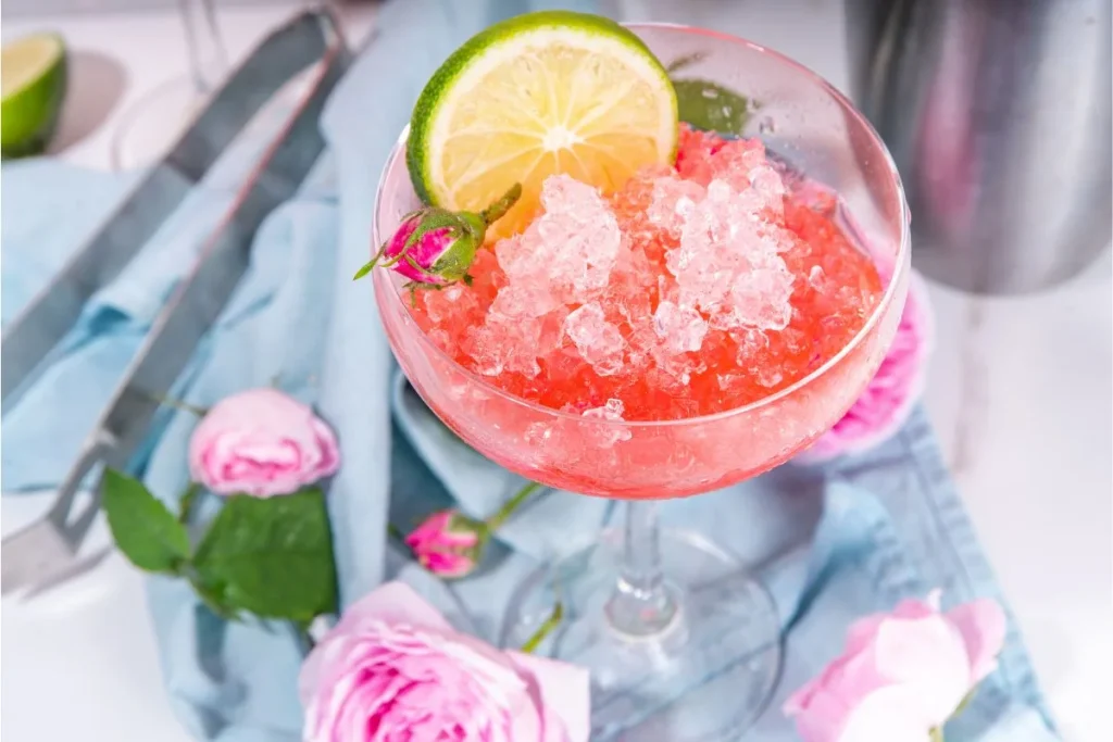 Pink frozen rose cocktail with crushed ice and a lime wheel in a coupe glass