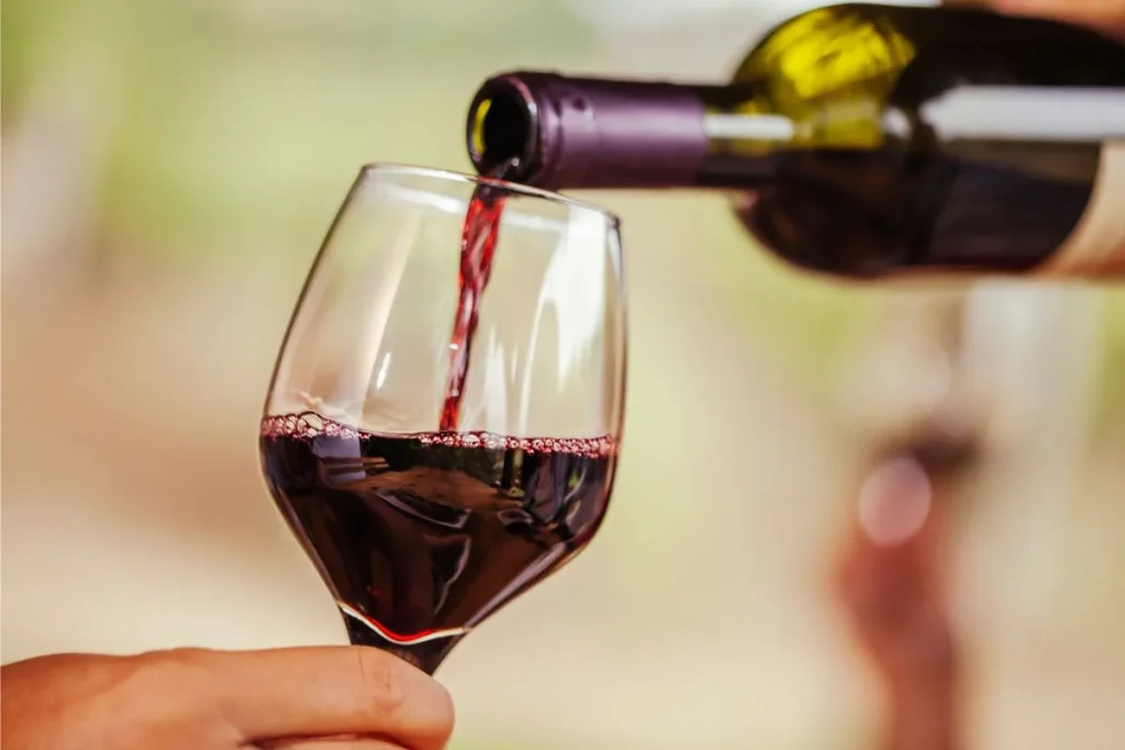 Red wine poured from a bottle into a glass held by a hand outdoors